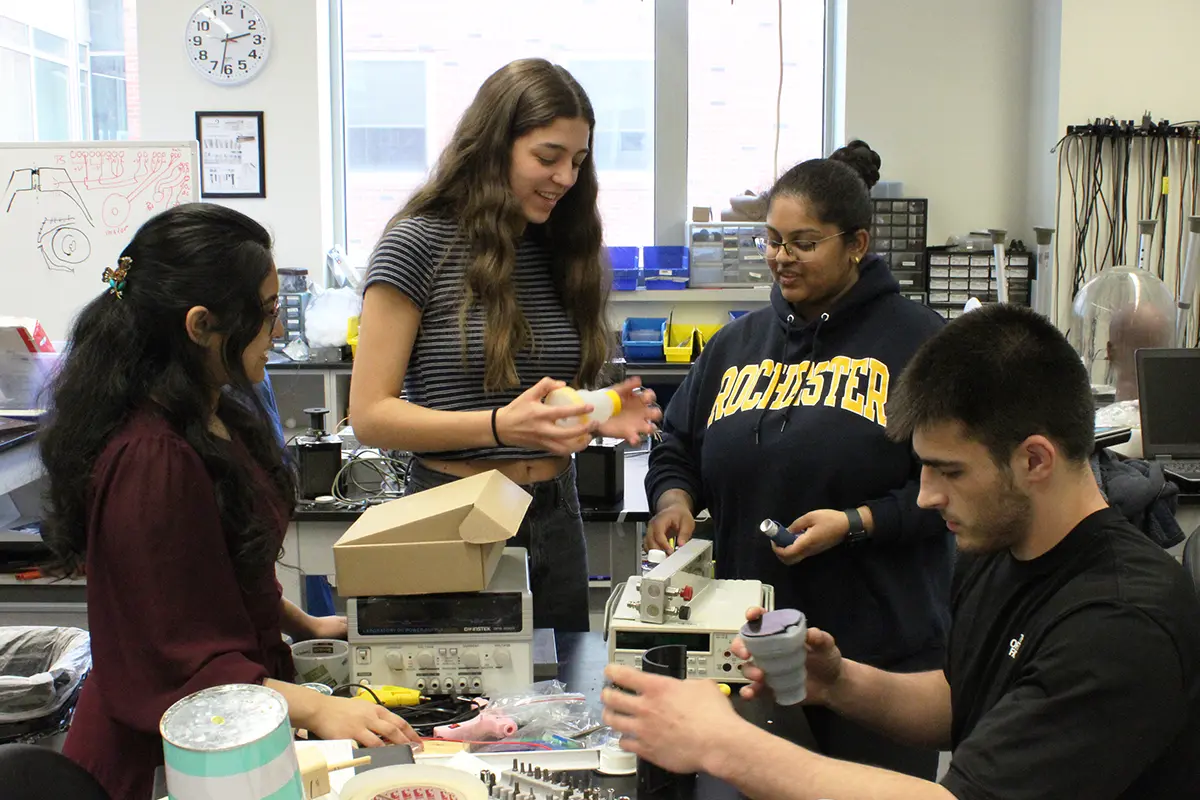 A group of four students work gather around a collapsible spacer for inhalers the team created.